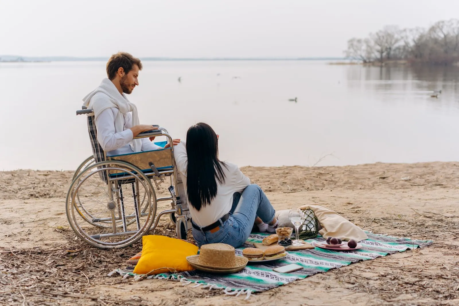 Support worker and an adult participant in a wheelchair enjoying a lakeside picnic outing.