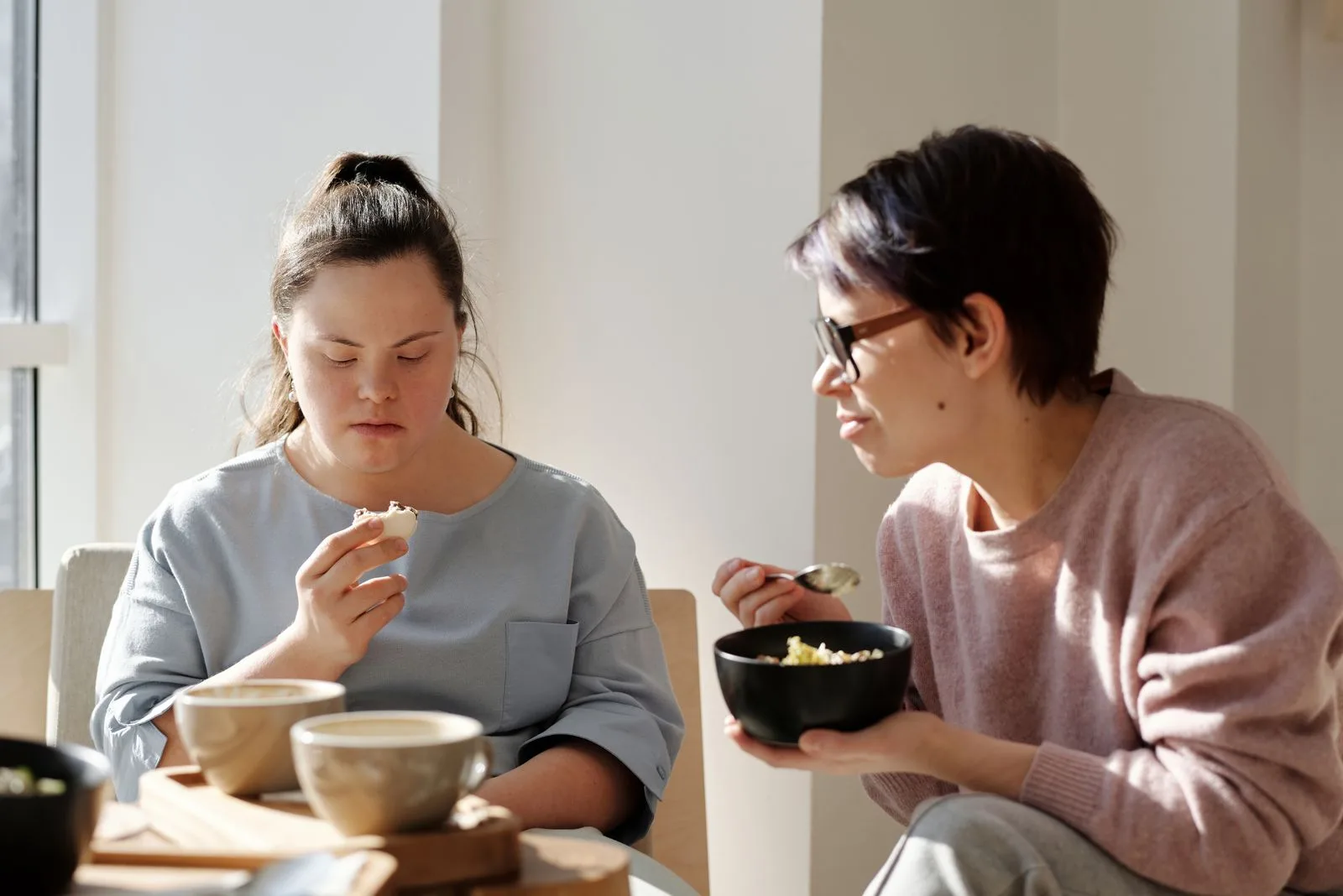Support worker and a resident with Down syndrome sharing breakfast together in a shared-home kitchen.