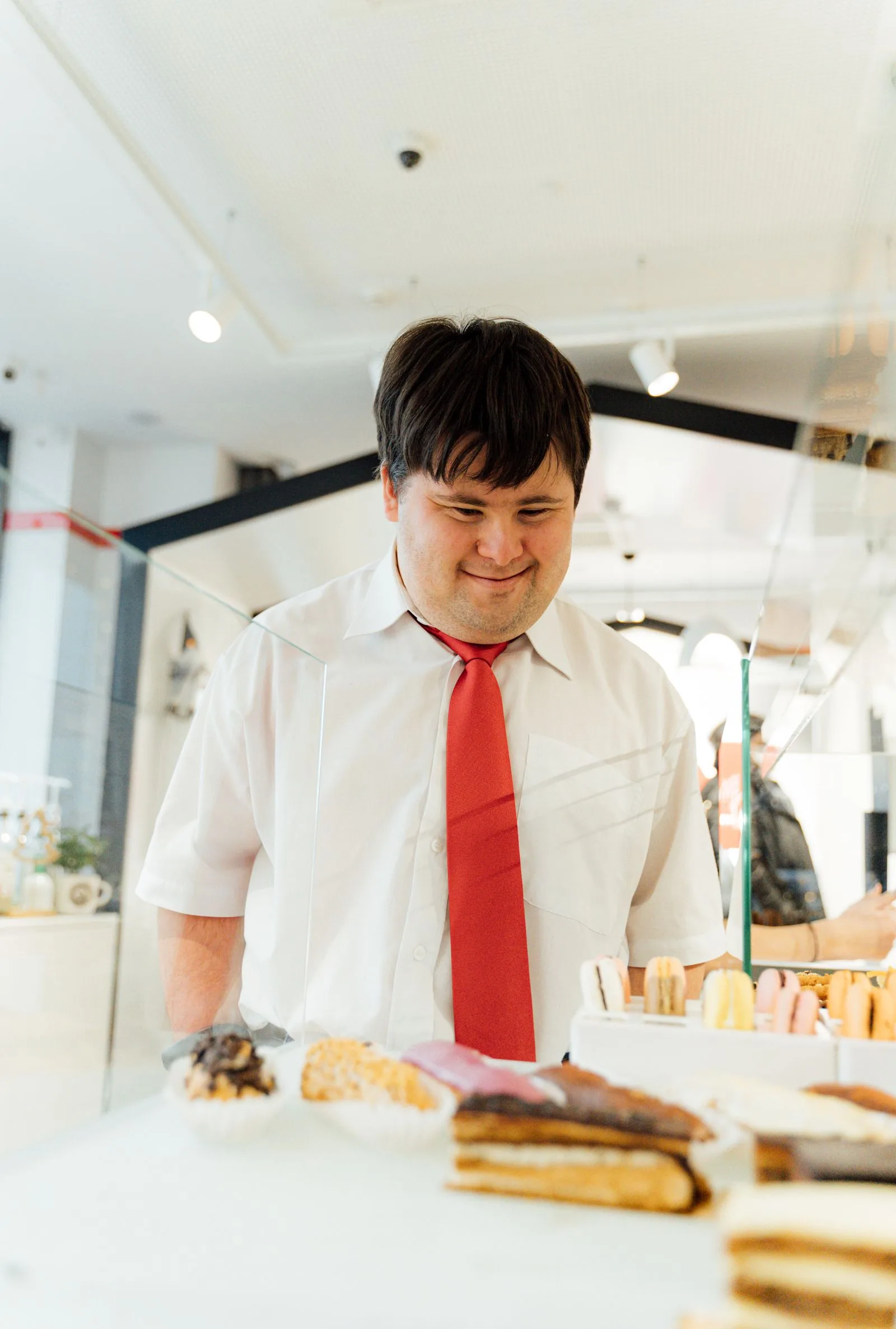 A young man with Down syndrome actively choosing pastries at a bakery display counter during an outing.